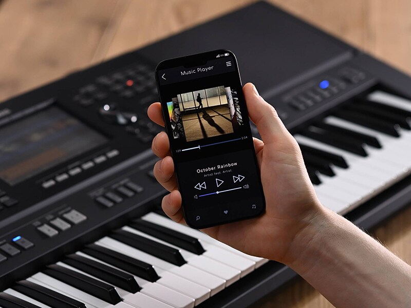 Yamaha Arranger Workstation PSR-SX920 und eine Hand, die ein Smartphone mit der Anzeige eines Musik-Players hält