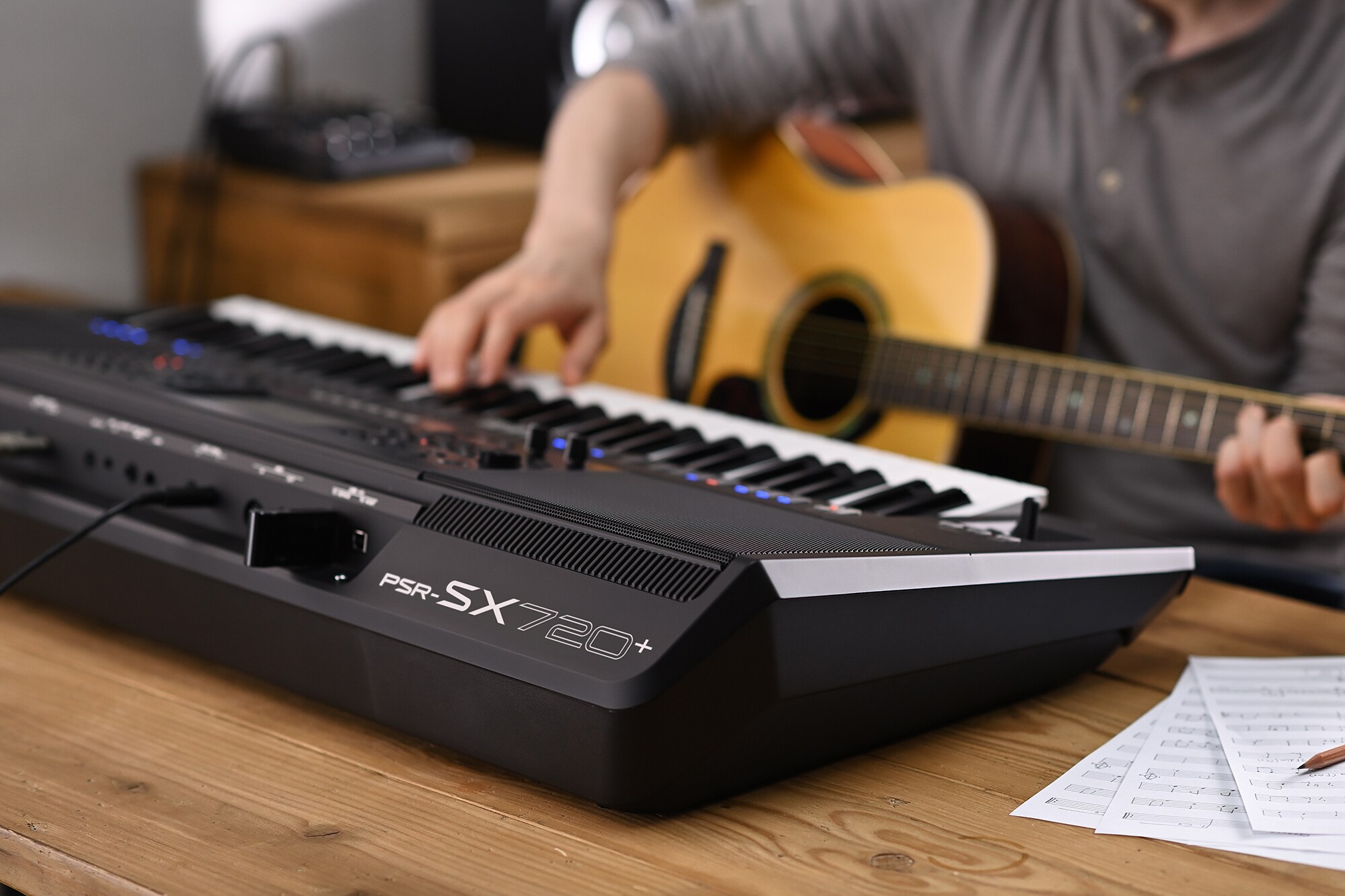 Foto einer Person, die auf der Yamaha Arranger Workstation PSR-SX720+ spielt und gleichzeitig eine Gitarre hält
